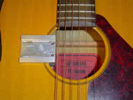 Image shows the overhead view of the mounting track attached to the guitar. The mount attaches like a clamp to the side of the guitar soundhole. The track is positioned perpendicularly and in close proximity to the guitar strings. Two ball protrusions stick out from the track and are used to guide the strumming component into place. 