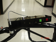 This picture displays how the device is attached to a rolling walker, using a bicycle light mount. The front of the device (and accordingly, the distance sensor) is pointed to where the patient’s torso would be vertically positioned. Additionally, the laser module is attached in similar fashion, and is shown to the left of the device with its gray power wire connected to the back of the main device. 