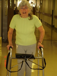 This is a picture of an individual with PD who tested out our device, and provided audio-visual feedback in the .mpeg clip attached. She is shown standing behind the walker, in the usual walking position. The fabric enclosures for the vibration motor wires are also seen, which are connected from the back of the main device to the motors which are situated on the handles of the walker. 