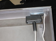 Image shows the handle of the lawnmower cord attracted to a magnet embedded in the Lexan® beam.  The lawnmower cord itself goes from the handle, through a hole in the beam, and to the opposite side of a flap.  A screw protrudes from a Lexan® support block to keep the shelf securely in place when the flap is lowered. 