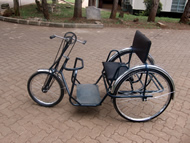 This figure shows the third generation of the Figure-Eight Drive installed on a standard APDK handcycle, in Nairobi, Kenya.  The system only requires modification of the tricycle’s fork and chains, leaving the rest identical to single-speed models. 