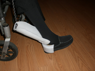 The image shows the final device in use by our client as a shoe helper.  The rigid, modified heel sleeve fits around the back of the shoe and prevents the shoe from folding beneath the foot.  A hinge attaches it to a modified shoehorn of much larger width, giving our client a location for placement of the heel.  Lastly, a string is attached through two holes drilled through the top of the shoehorn.  Our client pulls the string to rotate the shoehorn and guide the foot into the shoe.
