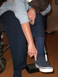 The image shows our client bending over and reaching to remove the back of the shoe from underneath the heel.  Our client reaches with her right arm across her body to her left foot.  This is the maximum extent of her flexibility and it is very uncomfortable and difficult for her to reach in this manner.  
