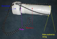 The image shows the final device design from behind.  The shoehorn (red) is now much longer with holes still drilled into the top for the string (yellow).  The hinge connection (purple arrow) to the heel sleeve (blue arrow) remains the same as in the previous prototype.  A final modification is the bracket (green arrow), which has the string laced through it when the device is used as a sock aid. 