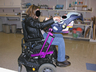 This picture shows the finished device installed and in use on the mother’s wheelchair.  From this right-side view, we can see the IPS extrusion mounted to the mother’s wheelchair and the adjustable frame riding along  it, supporting the purchased infant seat.   