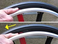 Figure shows the return spring attached to the perimeter of the wheel and the rotating member that the push rim attaches to.  An arrow indicates the backwards articulation of the push rim when braking.